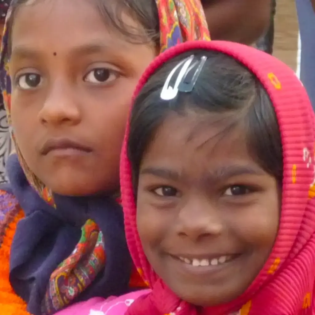 Zwei Kinder schauen in die Kamera. Ein Kind lächelt, das andere blickt ernster.